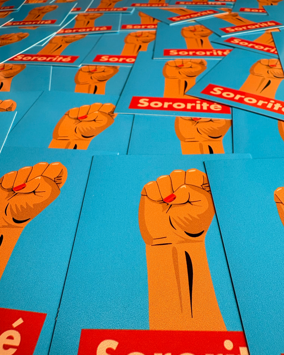 Stickers « Sororité » disposés côte à côte, avec un poing levé sur fond bleu et le texte sur un bandeau rouge.